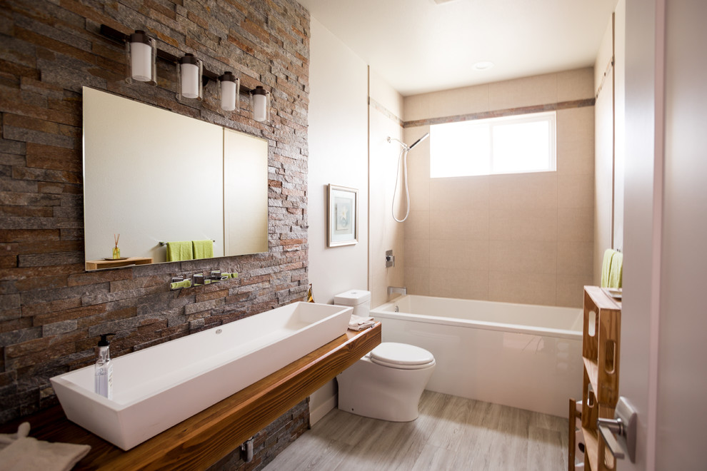 This is an example of a mid-sized contemporary kids bathroom in Seattle with open cabinets, brown cabinets, an alcove tub, a shower/bathtub combo, a one-piece toilet, beige tile, porcelain tile, beige walls, porcelain floors, a trough sink, wood benchtops, brown floor, a shower curtain and brown benchtops.