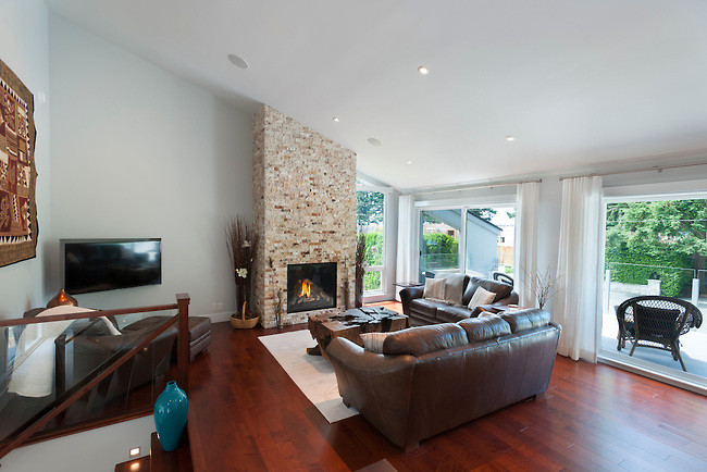 Design ideas for a mid-sized contemporary family room in Vancouver with dark hardwood floors, a wall-mounted tv, a hanging fireplace and a stone fireplace surround.