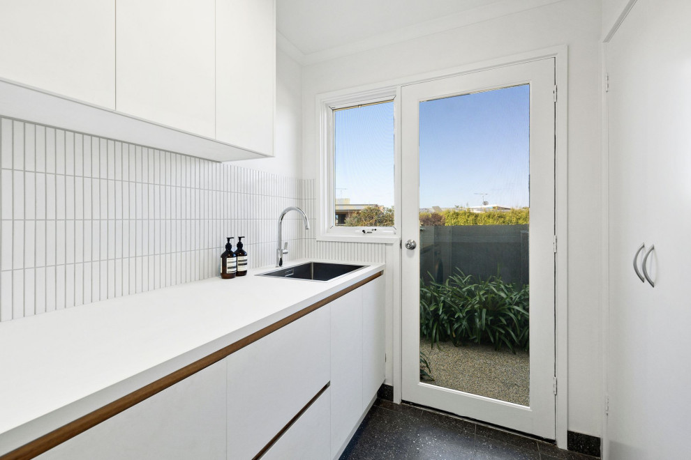 Photo of a medium sized modern galley separated utility room in Geelong with a single-bowl sink, flat-panel cabinets, white cabinets, composite countertops, white splashback, matchstick tiled splashback, white walls, porcelain flooring, a side by side washer and dryer, black floors and white worktops.