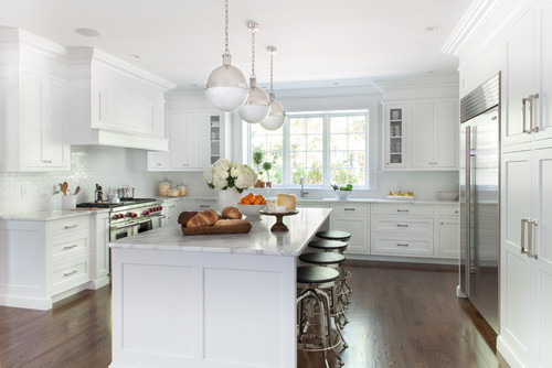 Bright white kitchen with shaker RTA cabinets, crown molding, marble-look island, pendant lights, stainless appliances, and hardwood floors.