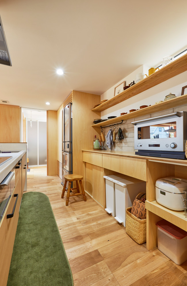 This is an example of an asian galley kitchen in Other with flat-panel cabinets, medium wood cabinets, white splashback, stainless steel appliances, medium hardwood floors, a peninsula, brown floor and white benchtop.