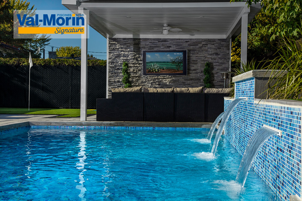 This is an example of a large modern backyard rectangular pool with a water feature and brick pavers.