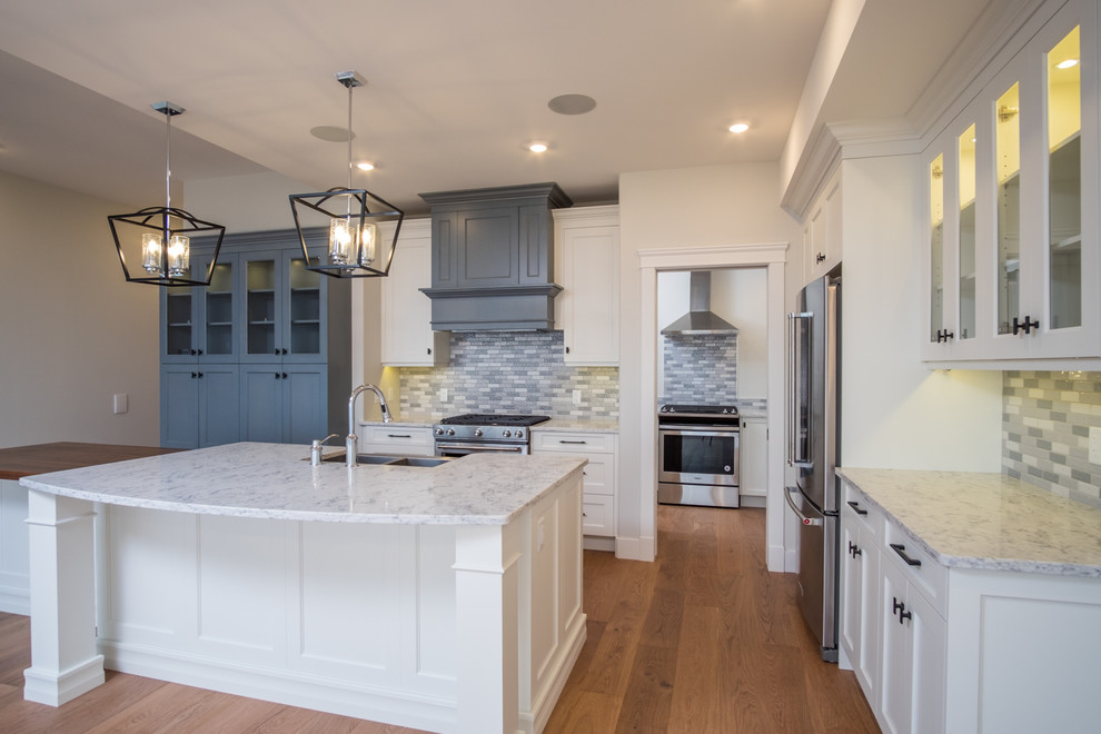 Open concept kitchen - mid-sized transitional l-shaped medium tone wood floor and brown floor open concept kitchen idea with a farmhouse sink, shaker cabinets, blue cabinets, quartzite countertops, multicolored backsplash, ceramic backsplash, stainless steel appliances, an island and white countertops