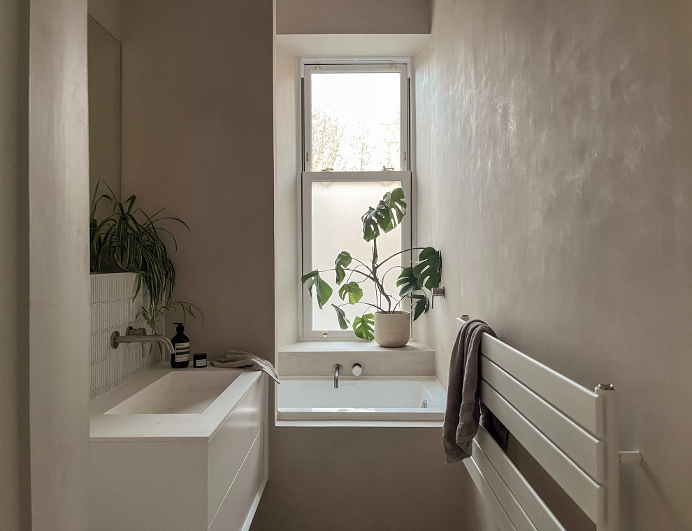 Idéer för att renovera ett litet skandinaviskt vit vitt badrum för barn, med släta luckor, vita skåp, ett platsbyggt badkar, en dusch/badkar-kombination, en vägghängd toalettstol, vit kakel, mosaik, beige väggar, ett väggmonterat handfat, bänkskiva i akrylsten, beiget golv och med dusch som är öppen