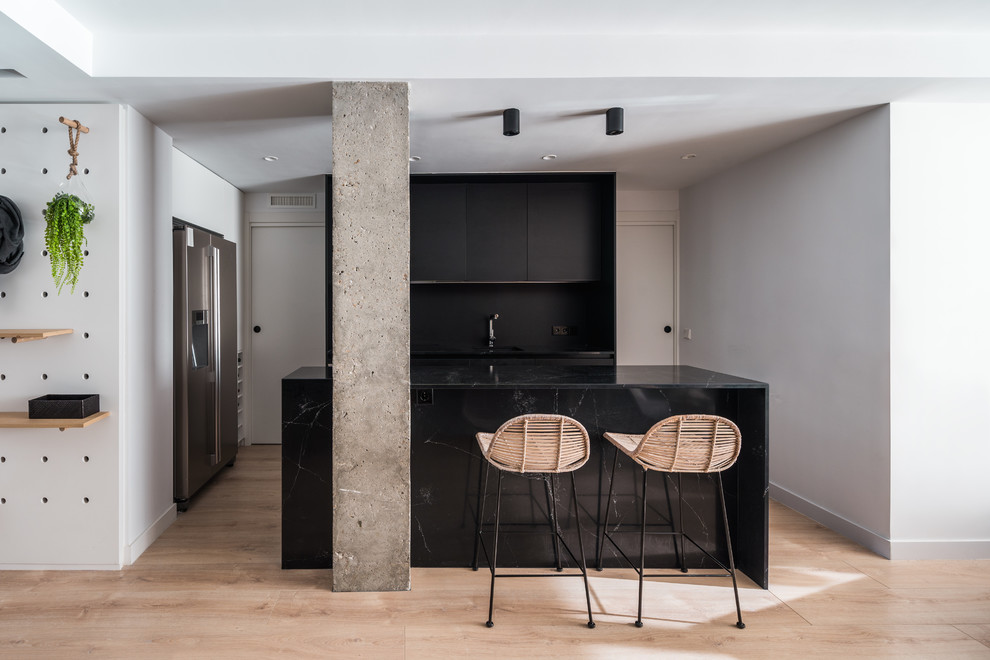 Design ideas for a contemporary l-shaped eat-in kitchen in Other with an undermount sink, flat-panel cabinets, black cabinets, black splashback, stainless steel appliances, light hardwood floors, with island, beige floor and black benchtop.