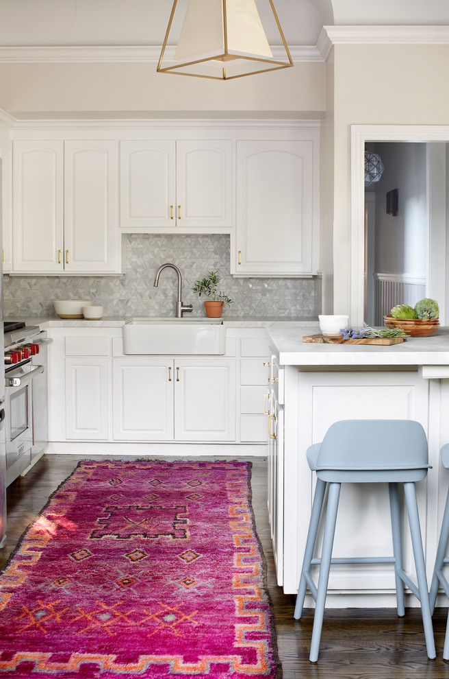This is an example of a transitional l-shaped kitchen in San Francisco with raised-panel cabinets, white cabinets, grey splashback, mosaic tile splashback, stainless steel appliances, dark hardwood floors, with island, brown floor and a farmhouse sink.