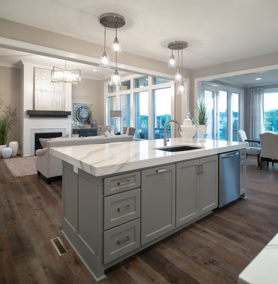 This is an example of an arts and crafts galley open plan kitchen in Kansas City with a drop-in sink, white cabinets, white splashback, stainless steel appliances, medium hardwood floors, with island, brown floor and white benchtop.