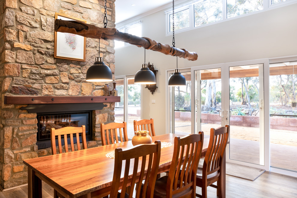 Photo of a mid-sized contemporary open plan dining in Perth with white walls, laminate floors, a two-sided fireplace, a stone fireplace surround, brown floor and vaulted.
