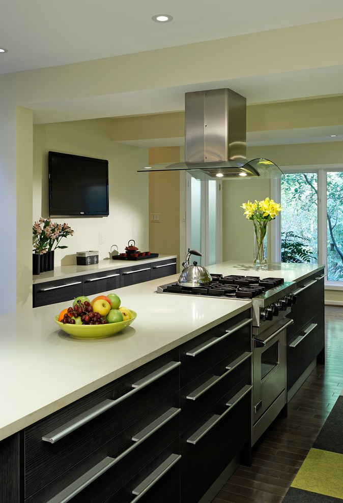 Photo of a mid-sized modern galley eat-in kitchen in DC Metro with an undermount sink, flat-panel cabinets, medium wood cabinets, quartz benchtops, grey splashback, glass sheet splashback, stainless steel appliances, medium hardwood floors, with island, brown floor and white benchtop.