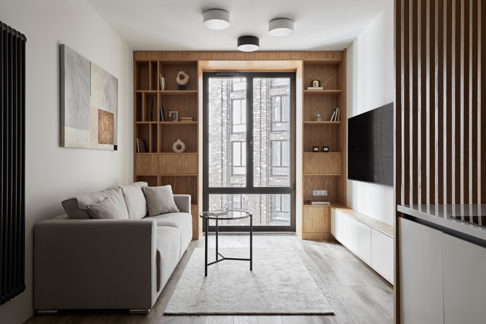 Стильный дизайн: гостиная комната среднего размера в современном стиле с белыми стенами, паркетным полом среднего тона, телевизором на стене и коричневым полом - последний тренд