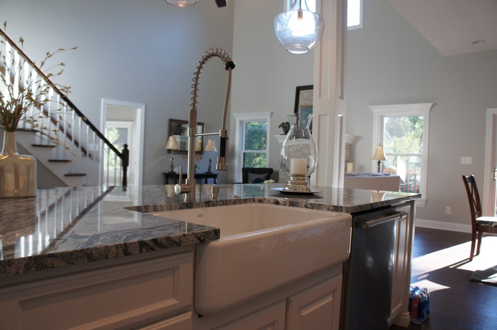 Open concept kitchen - transitional single-wall dark wood floor open concept kitchen idea with a farmhouse sink, raised-panel cabinets, white cabinets, granite countertops, white backsplash, stainless steel appliances and an island