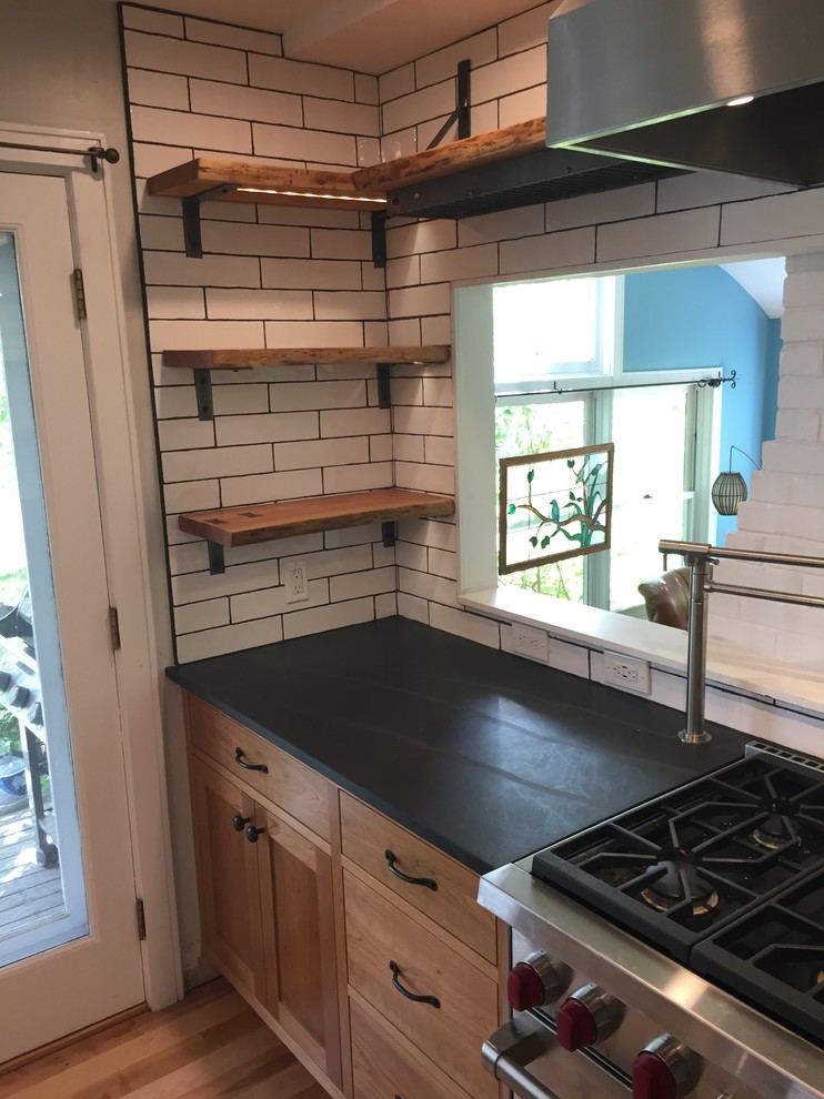 Photo of a contemporary open plan kitchen in Portland Maine with a farmhouse sink, shaker cabinets, light wood cabinets, white splashback, ceramic splashback, stainless steel appliances, light hardwood floors, with island and grey benchtop.