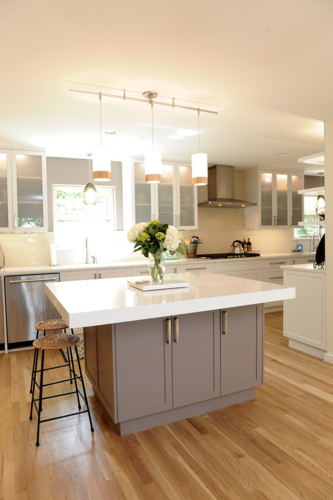 Design ideas for a mid-sized transitional l-shaped kitchen in Dallas with an undermount sink, shaker cabinets, white cabinets, beige splashback, matchstick tile splashback, stainless steel appliances, light hardwood floors, with island, beige floor and white benchtop.
