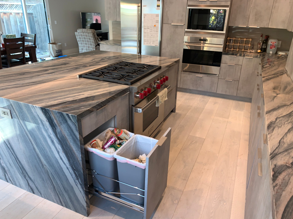 Large modern u-shaped open plan kitchen in San Francisco with a farmhouse sink, flat-panel cabinets, distressed cabinets, marble benchtops, beige splashback, porcelain splashback, stainless steel appliances, light hardwood floors, with island, beige floor and green benchtop.