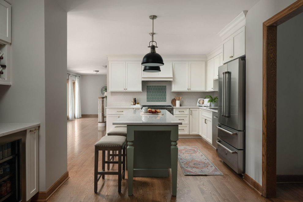 This is an example of a medium sized traditional l-shaped kitchen/diner in Chicago with a submerged sink, flat-panel cabinets, white cabinets, engineered stone countertops, beige splashback, ceramic splashback, stainless steel appliances, medium hardwood flooring, an island and white worktops.
