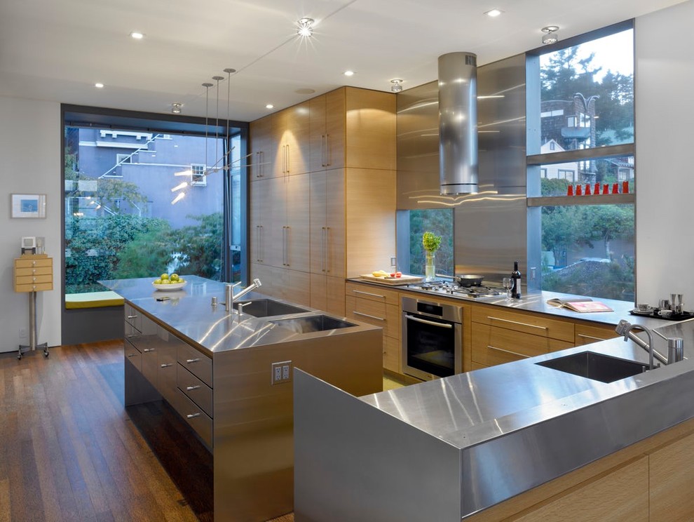 Photo of a large l-shaped eat-in kitchen in San Francisco with an undermount sink, flat-panel cabinets, light wood cabinets, stainless steel benchtops, metallic splashback, window splashback, panelled appliances, cork floors, with island and brown floor.