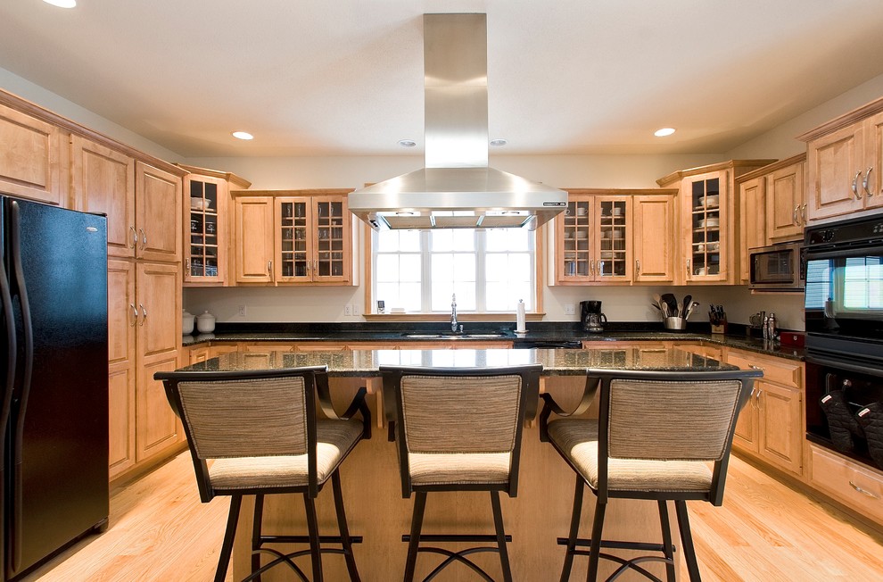 Example of a transitional light wood floor kitchen design with a double-bowl sink, raised-panel cabinets, light wood cabinets, granite countertops, black appliances and an island
