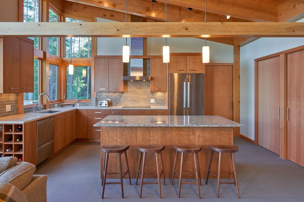 This is an example of a mid-sized contemporary l-shaped open plan kitchen in Seattle with an undermount sink, flat-panel cabinets, medium wood cabinets, stainless steel appliances, with island, solid surface benchtops, grey splashback, ceramic splashback, concrete floors and brown floor.