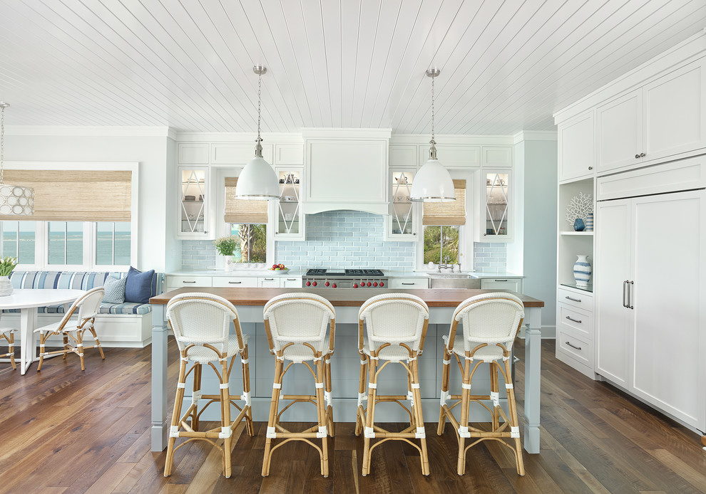 This is an example of a beach style l-shaped kitchen in Charleston with a farmhouse sink, shaker cabinets, white cabinets, grey splashback, stainless steel appliances, dark hardwood floors, with island, brown floor and white benchtop.