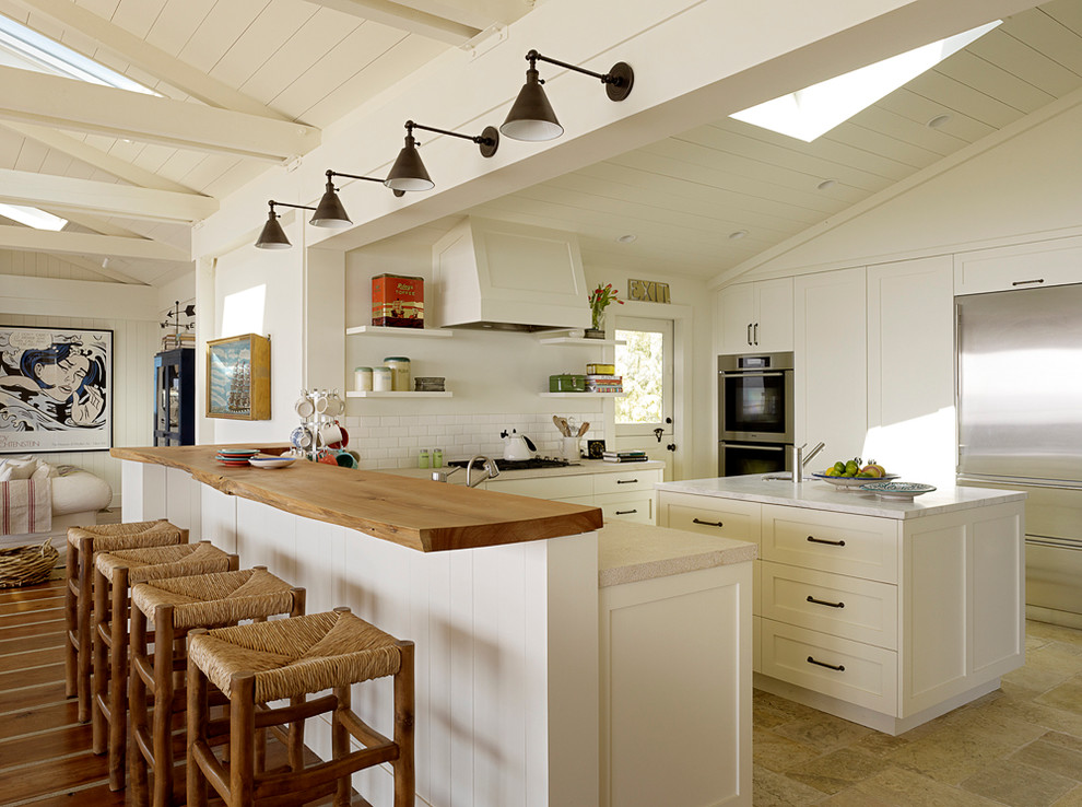 Large beach style u-shaped open plan kitchen in San Francisco with shaker cabinets, white cabinets, white splashback, subway tile splashback, stainless steel appliances, with island, an undermount sink, quartzite benchtops, ceramic floors and beige floor.