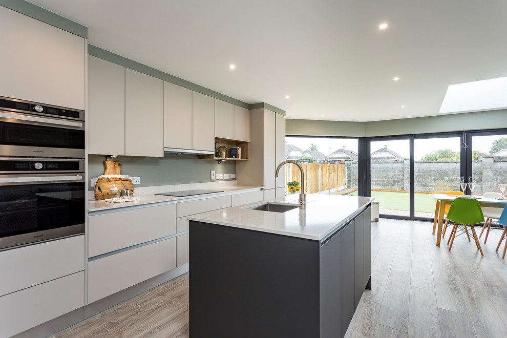This is an example of a mid-sized contemporary galley open plan kitchen in Other with flat-panel cabinets, grey cabinets, solid surface benchtops, stainless steel appliances, medium hardwood floors, with island, grey floor, white benchtop, an undermount sink and grey splashback.
