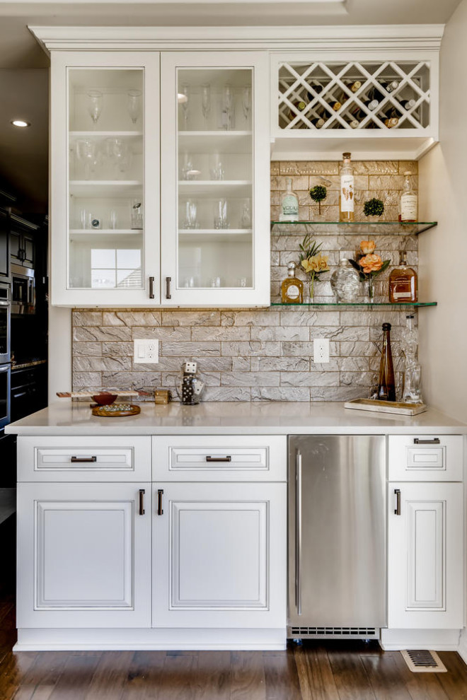 This is an example of a mid-sized transitional single-wall home bar in Denver with glass-front cabinets, white cabinets, quartz benchtops, grey splashback, subway tile splashback and white benchtop.