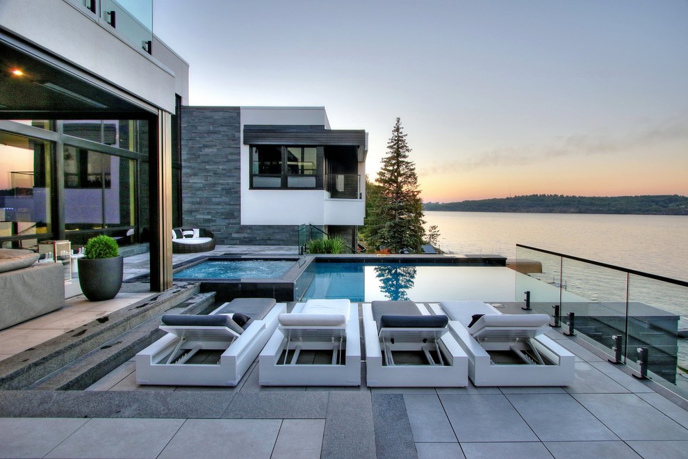 Photo of a mid-sized contemporary backyard rectangular infinity pool in Toronto with a hot tub and natural stone pavers.