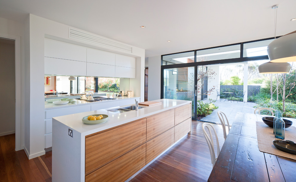 This is an example of a contemporary galley eat-in kitchen in Canberra - Queanbeyan with a double-bowl sink, flat-panel cabinets, white cabinets, medium hardwood floors and with island.