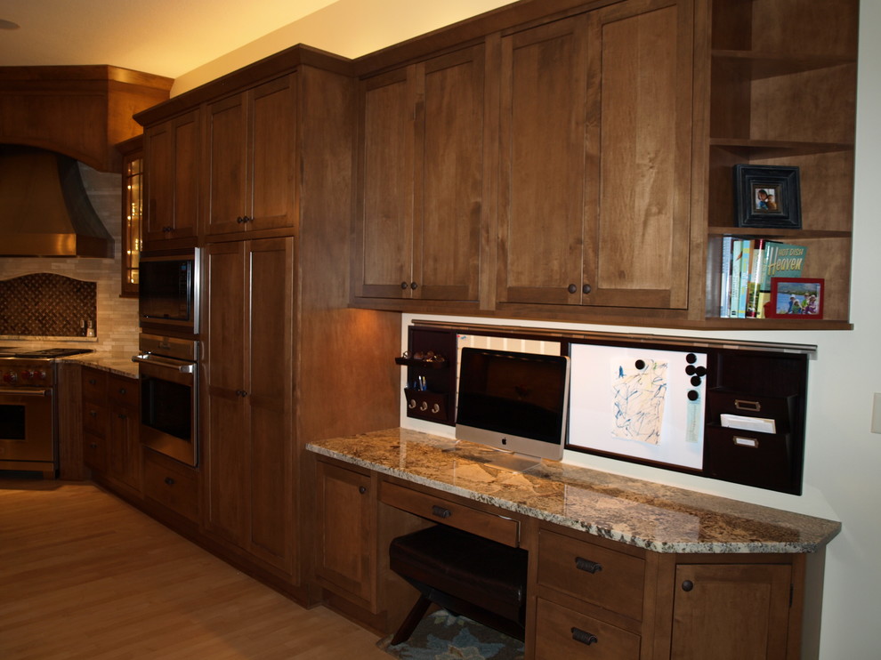 This is an example of a large country eat-in kitchen in Minneapolis with shaker cabinets, medium wood cabinets, granite benchtops, brown splashback, stone tile splashback, stainless steel appliances, light hardwood floors and with island.
