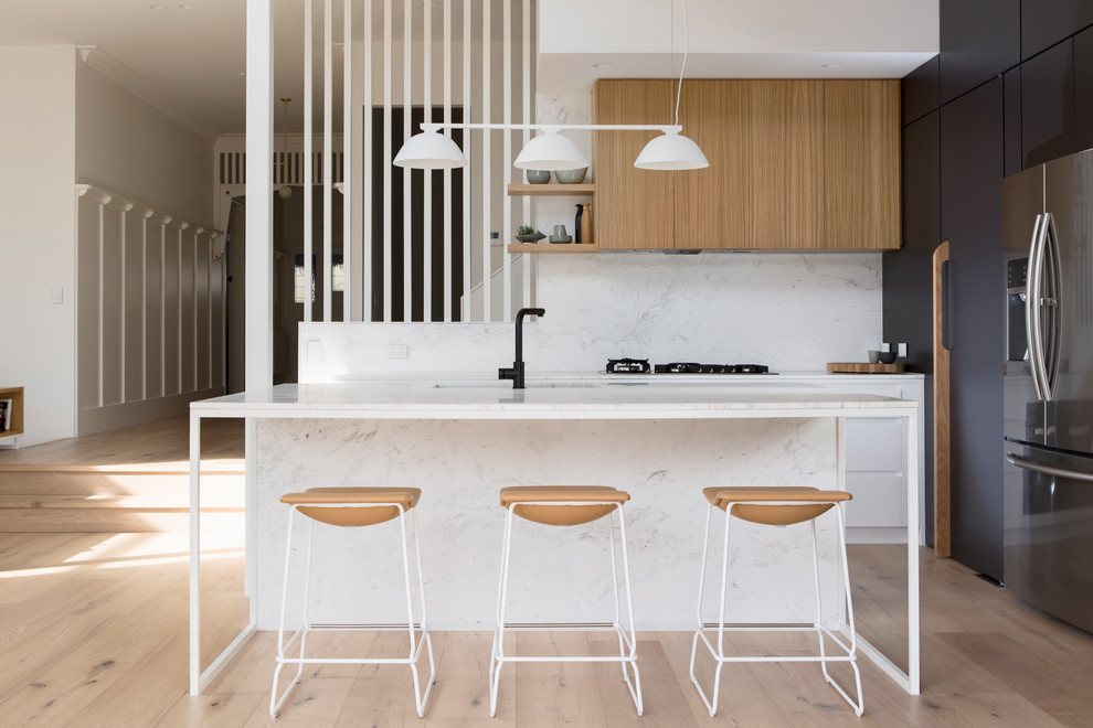 This is an example of a contemporary l-shaped kitchen in Melbourne with flat-panel cabinets, white splashback, stainless steel appliances, light hardwood floors, with island and beige floor.