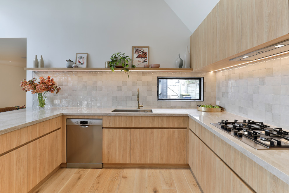 Mid-sized modern galley kitchen pantry in Auckland with grey splashback, stone tile splashback, stainless steel appliances, laminate floors and with island.