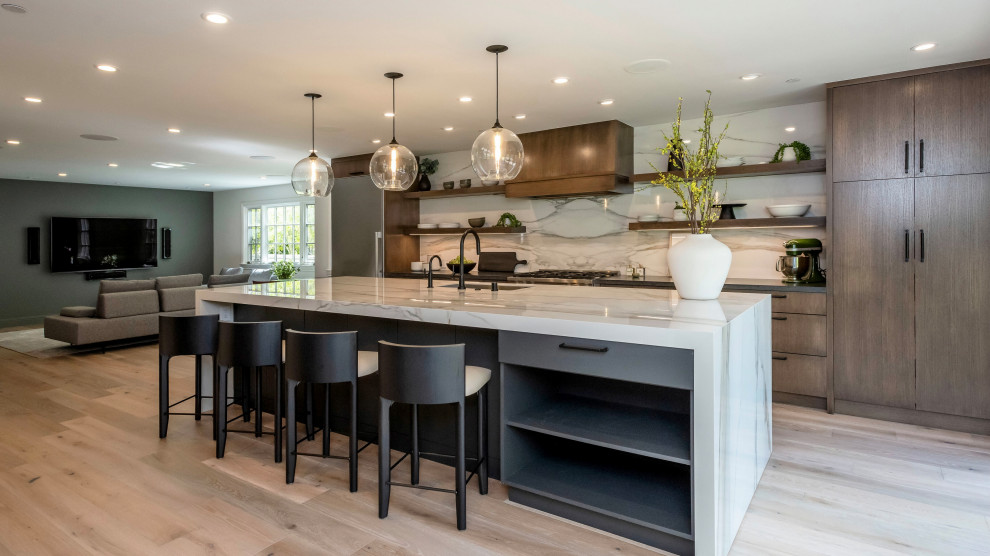 Contemporary single-wall open plan kitchen in San Francisco with a submerged sink, flat-panel cabinets, medium wood cabinets, engineered stone countertops, white splashback, stone slab splashback, stainless steel appliances, light hardwood flooring, an island, brown floors and multicoloured worktops.
