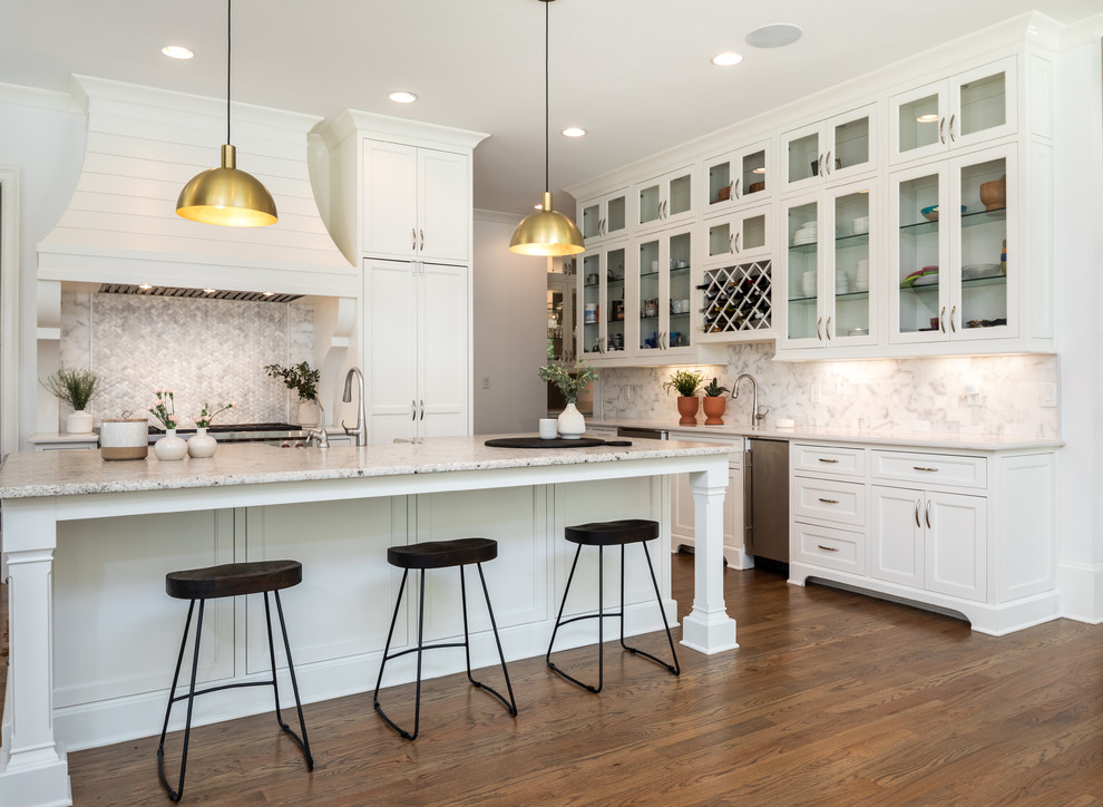 This is an example of a large beach style u-shaped eat-in kitchen in Los Angeles with shaker cabinets, white cabinets, multi-coloured splashback, stainless steel appliances, medium hardwood floors, with island, multi-coloured benchtop, a farmhouse sink, granite benchtops, marble splashback and brown floor.