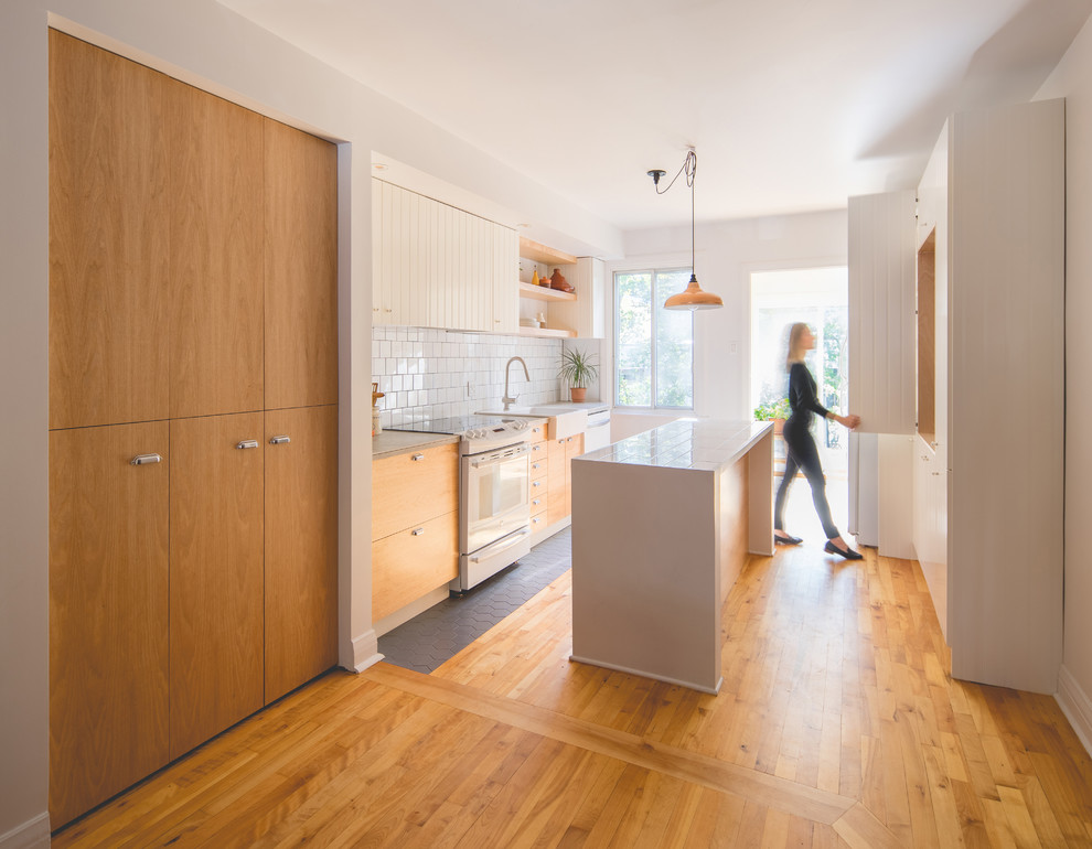 Mid-sized contemporary galley eat-in kitchen in Montreal with a single-bowl sink, flat-panel cabinets, medium wood cabinets, tile benchtops, white splashback, ceramic splashback, white appliances, ceramic floors, with island and grey floor.