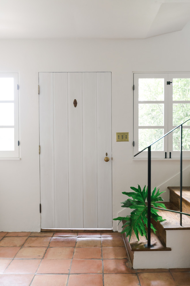 This is an example of a mid-sized foyer in Los Angeles with white walls, terra-cotta floors, a single front door, a white front door and red floor.