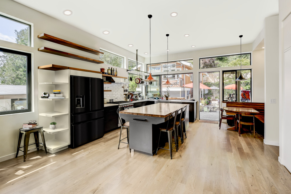 Open concept kitchen - large contemporary l-shaped light wood floor open concept kitchen idea in Seattle with a farmhouse sink, flat-panel cabinets, gray cabinets, wood countertops, white backsplash, subway tile backsplash, black appliances, an island and white countertops