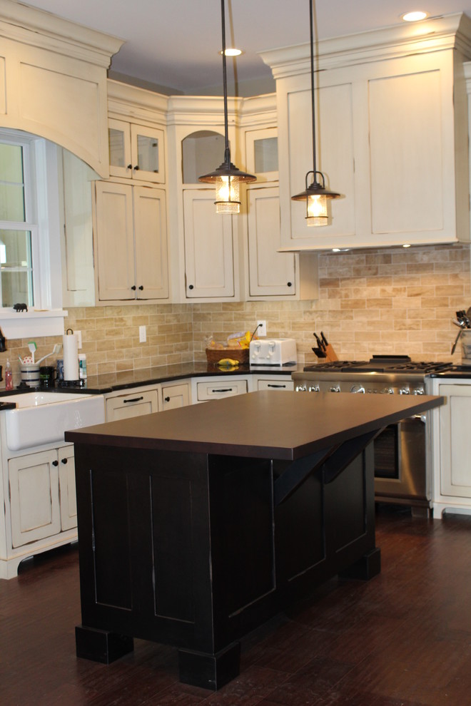 Photo of a country l-shaped eat-in kitchen in Indianapolis with a farmhouse sink, shaker cabinets, distressed cabinets, quartzite benchtops, beige splashback, ceramic splashback, stainless steel appliances, medium hardwood floors and a peninsula.