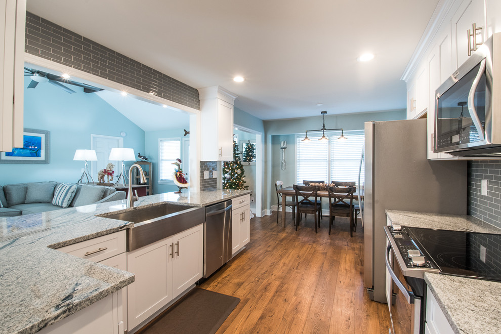 This is an example of a mid-sized country galley eat-in kitchen in Charleston with a farmhouse sink, shaker cabinets, white cabinets, marble benchtops, grey splashback, glass tile splashback, stainless steel appliances, medium hardwood floors and with island.