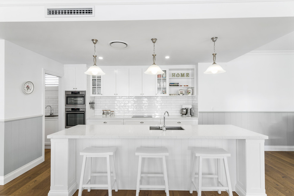 Design ideas for a large traditional galley kitchen pantry in Gold Coast - Tweed with an undermount sink, shaker cabinets, white cabinets, quartz benchtops, white splashback, subway tile splashback, stainless steel appliances, linoleum floors, with island, brown floor and yellow benchtop.
