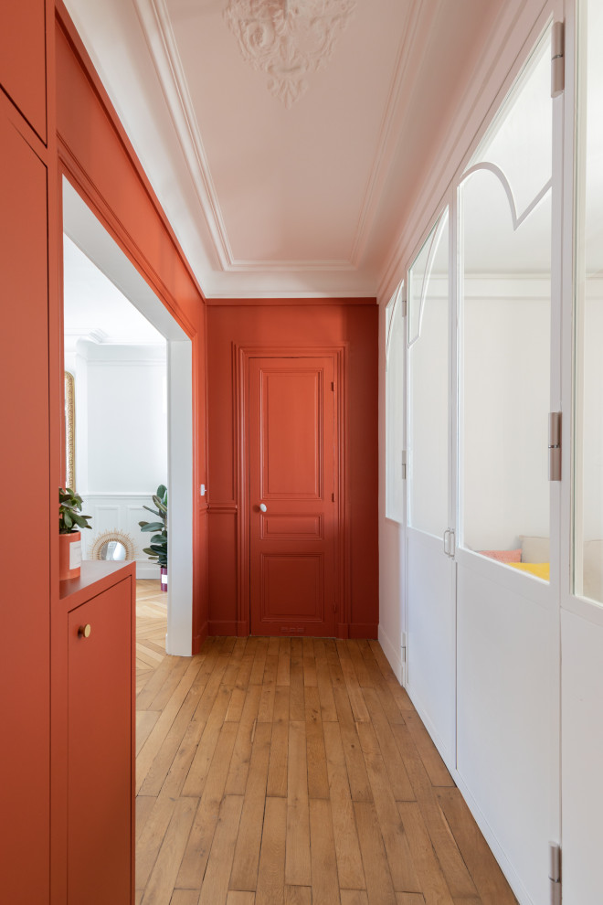 Aménagement d'une entrée contemporaine de taille moyenne avec un mur rouge, un sol en bois brun, une porte simple, une porte rouge, un sol marron et un couloir.