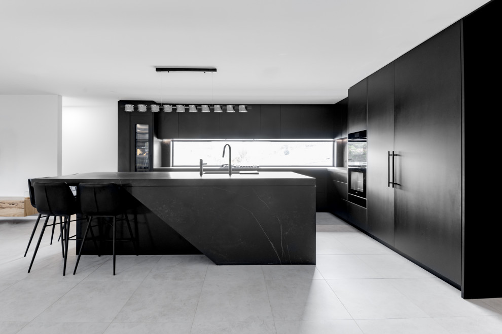 Large modern l-shaped enclosed kitchen in Central Coast with a submerged sink, flat-panel cabinets, black cabinets, engineered stone countertops, black splashback, engineered quartz splashback, black appliances, porcelain flooring, an island, grey floors, black worktops and a drop ceiling.