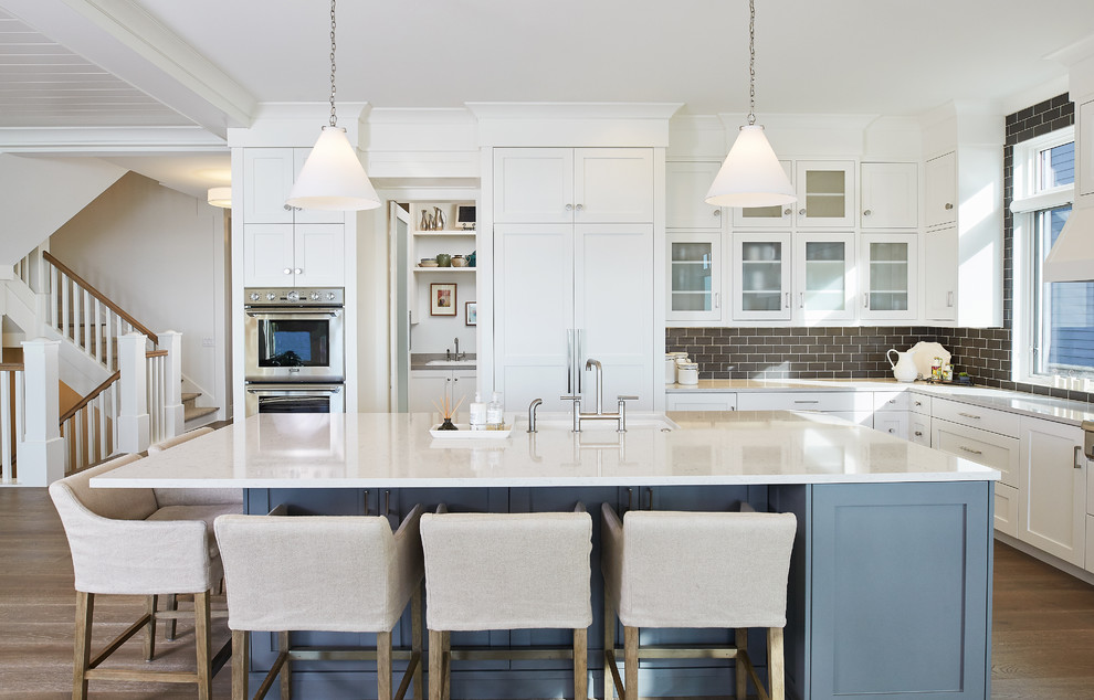 This is an example of a beach style l-shaped open plan kitchen in Grand Rapids with shaker cabinets, white cabinets, brown splashback, subway tile splashback, stainless steel appliances, medium hardwood floors and with island.