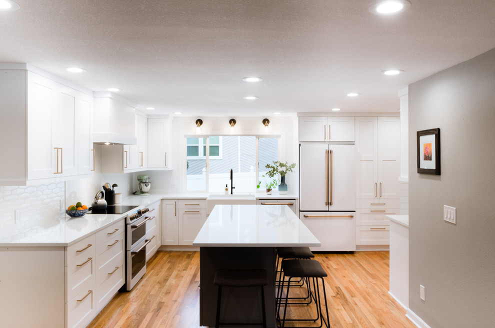 Photo of a mid-sized modern l-shaped eat-in kitchen in Portland with a farmhouse sink, shaker cabinets, white cabinets, quartz benchtops, white splashback, marble splashback, white appliances, light hardwood floors, with island and white benchtop.