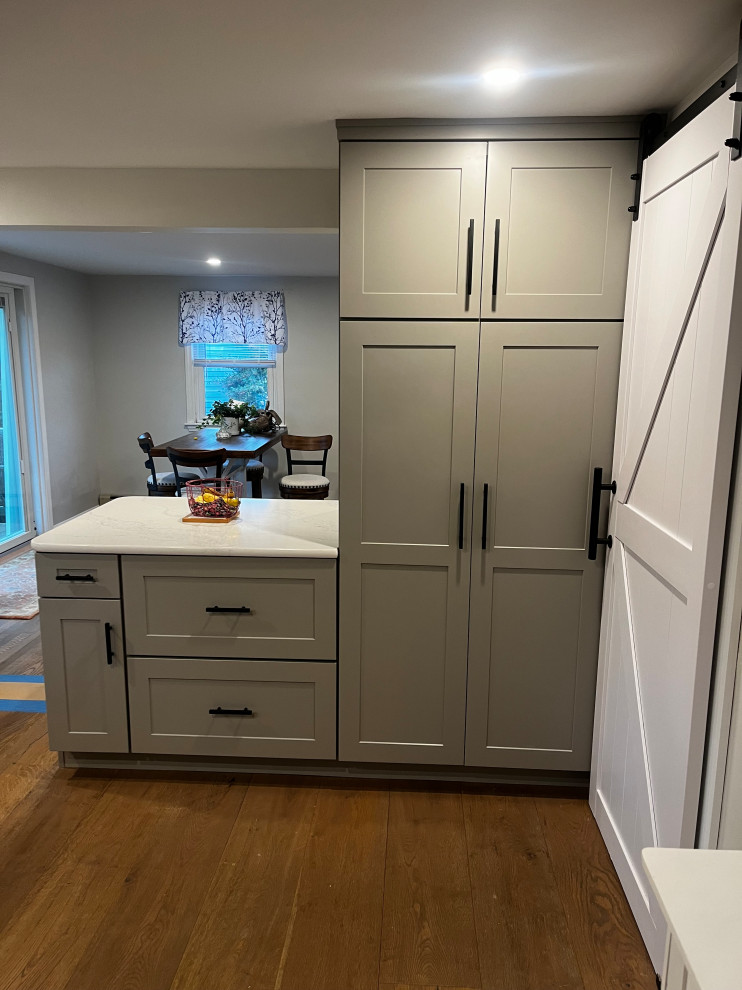 Mid-sized transitional u-shaped light wood floor and brown floor enclosed kitchen photo in Boston with an undermount sink, shaker cabinets, gray cabinets, quartz countertops, white backsplash, quartz backsplash, stainless steel appliances, a peninsula and white countertops