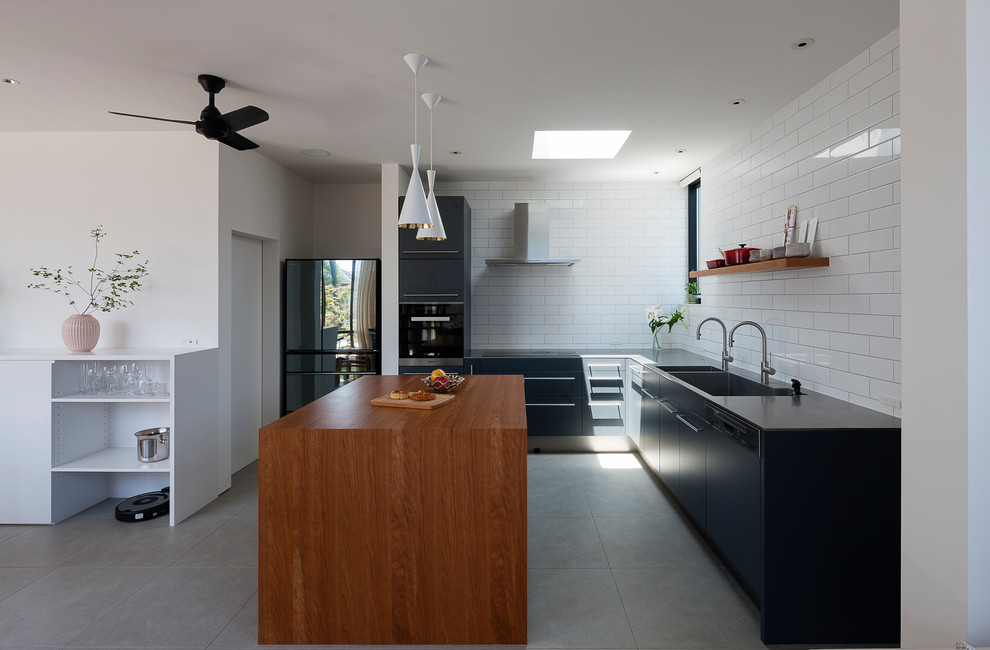 Photo of a large contemporary l-shaped open plan kitchen in Other with an undermount sink, flat-panel cabinets, black cabinets, stainless steel benchtops, white splashback, ceramic splashback, stainless steel appliances, ceramic floors, with island and grey floor.