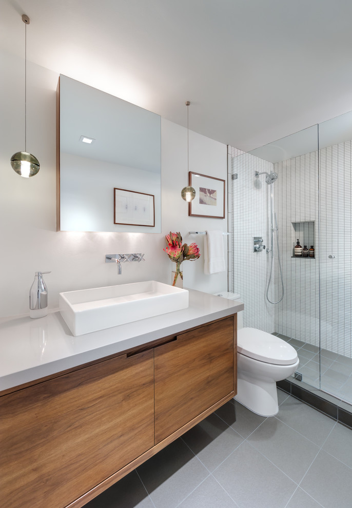 This is an example of a small contemporary 3/4 bathroom in Los Angeles with a vessel sink, medium wood cabinets, engineered quartz benchtops, an alcove shower, a one-piece toilet, white tile, ceramic tile, white walls, porcelain floors and grey benchtops.