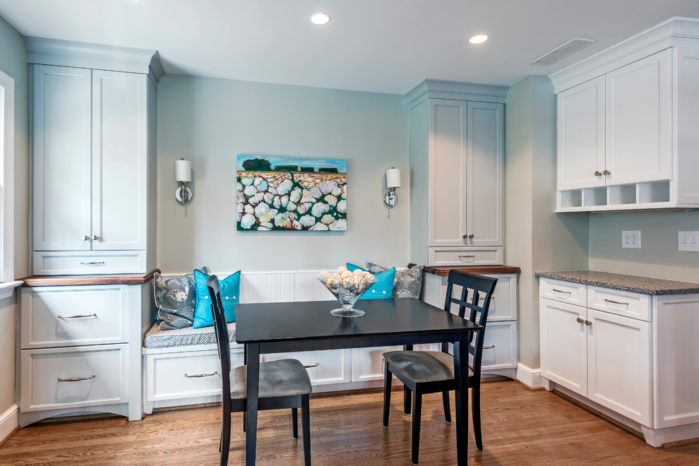 Large transitional l-shaped medium tone wood floor eat-in kitchen photo with a farmhouse sink, recessed-panel cabinets, white cabinets, stainless steel appliances, granite countertops, gray backsplash, subway tile backsplash and an island