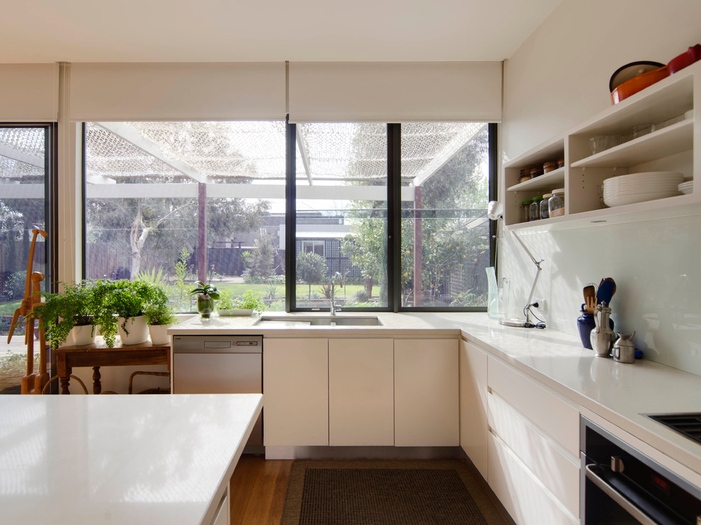 Design ideas for a mid-sized contemporary u-shaped eat-in kitchen in Melbourne with an undermount sink, flat-panel cabinets, white cabinets, quartz benchtops, white splashback, glass sheet splashback, black appliances, light hardwood floors and with island.
