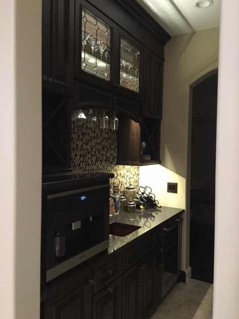 This is an example of a mid-sized traditional single-wall wet bar in Wichita with an undermount sink, raised-panel cabinets, dark wood cabinets, granite benchtops, multi-coloured splashback, mosaic tile splashback and medium hardwood floors.