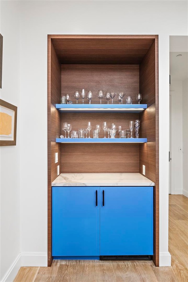 Photo of a small contemporary single-wall home bar in San Francisco with no sink, flat-panel cabinets, blue cabinets, marble benchtops, brown splashback, timber splashback, light hardwood floors, beige floor and white benchtop.